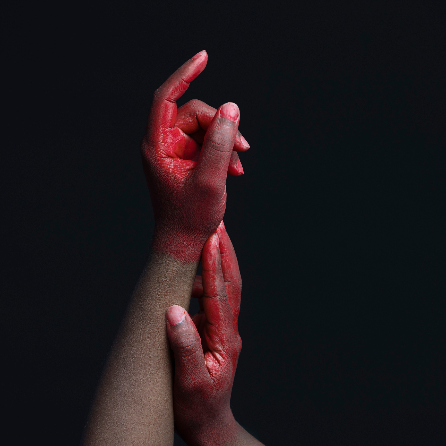 hands of a Black person, artfully posed, covered in red paint, against a black background
