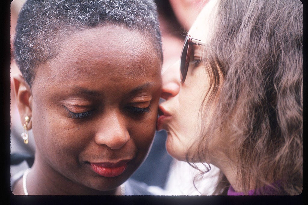 white woman with brown hair kisses black woman with short hair and gold earrings looking down.