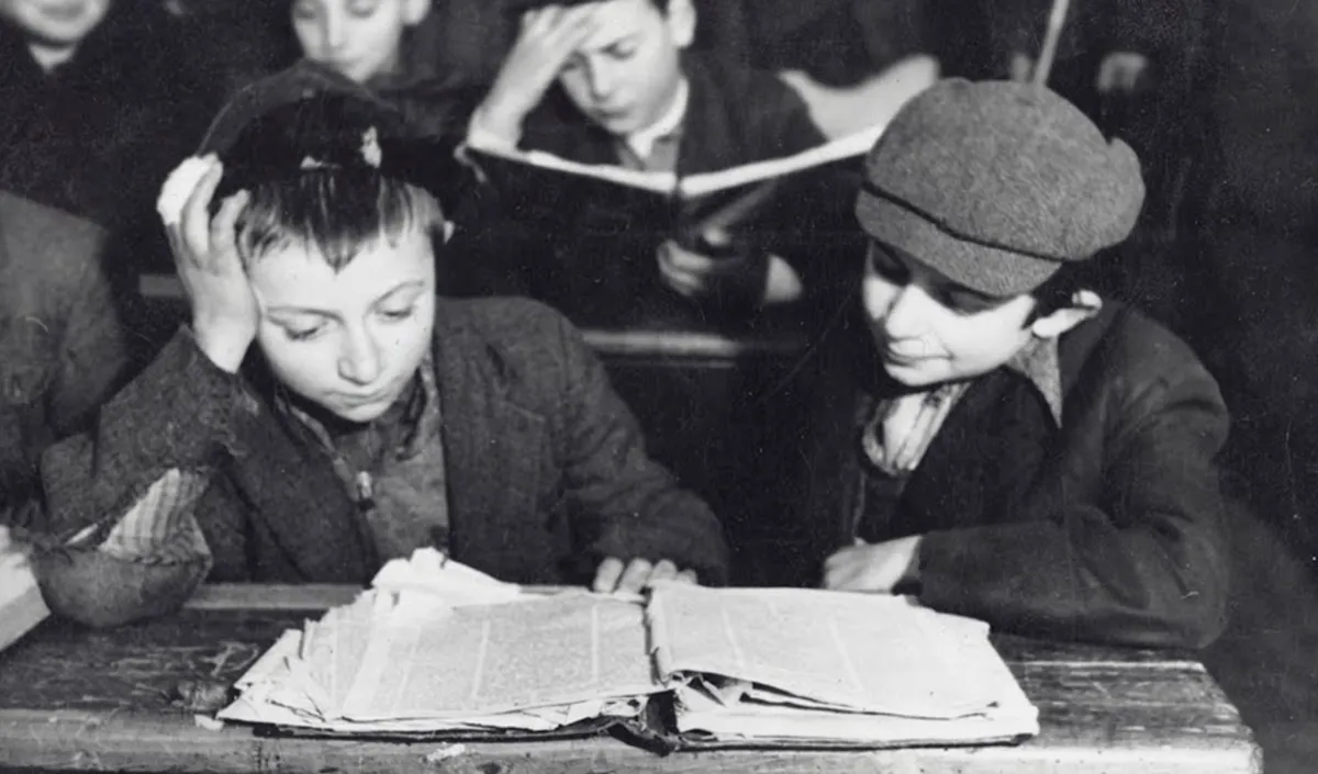 Two young kids in black and white studying a tattered Talmud together