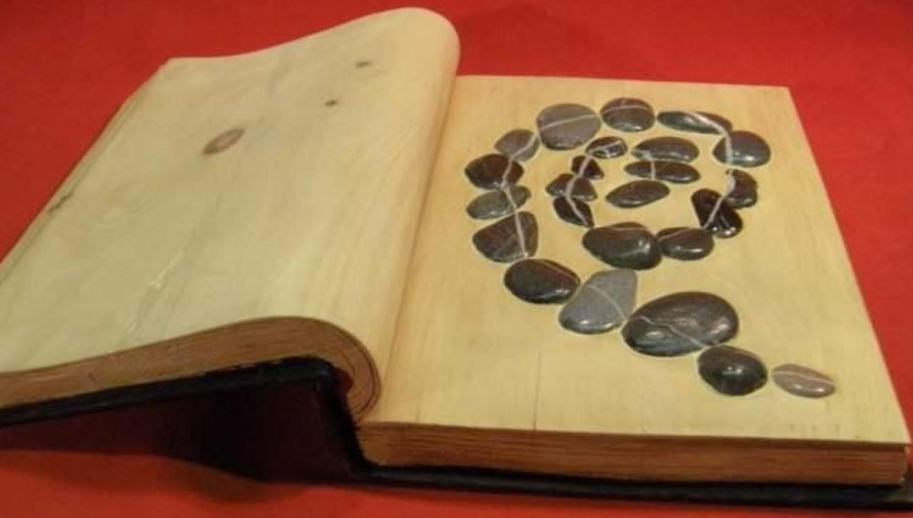 Wooden sculpture of a book with river stones spiraled inside 