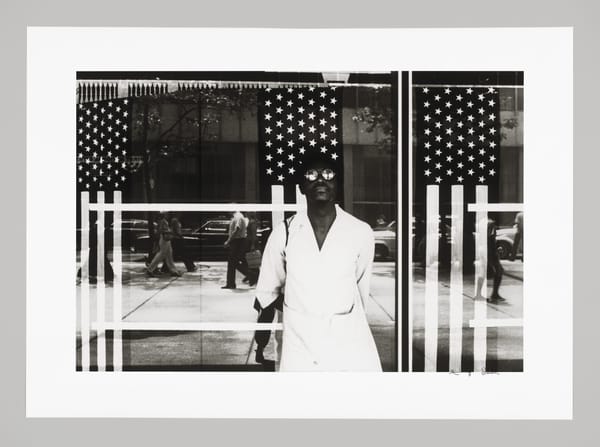 Photo of a Black person, with the reflection of US Flags seen behind them in the window